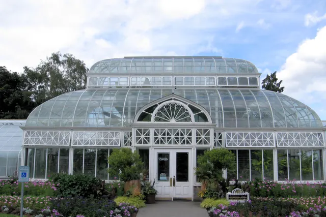 The white-framed glass conservatory in Volunteer Park, its domed roof over double doors, with purple and pink flowers along the path.