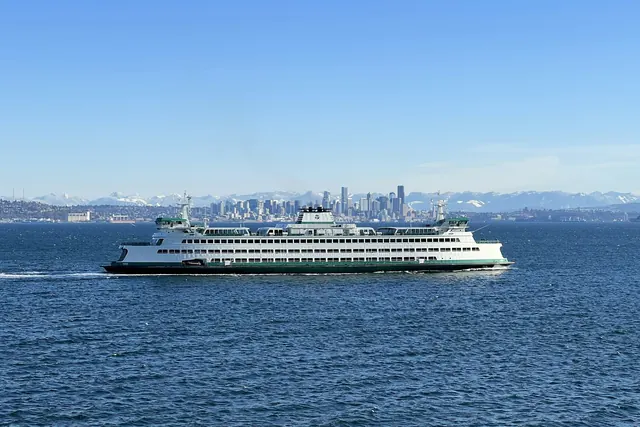 A white and green state ferry crossing deep blue water, with the city skyline and snowy mountains on the horizon.