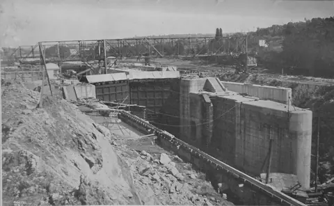 A deep concrete lock chamber with tall walls and gate housings, a steel crane gantry overhead and a rocky slope in front.