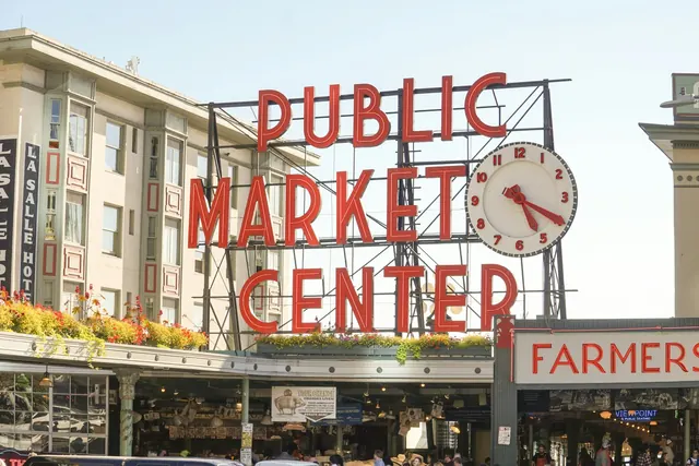 Large red letters reading Public Market Center beside a round white clock, above the market arcade under a pale sky.